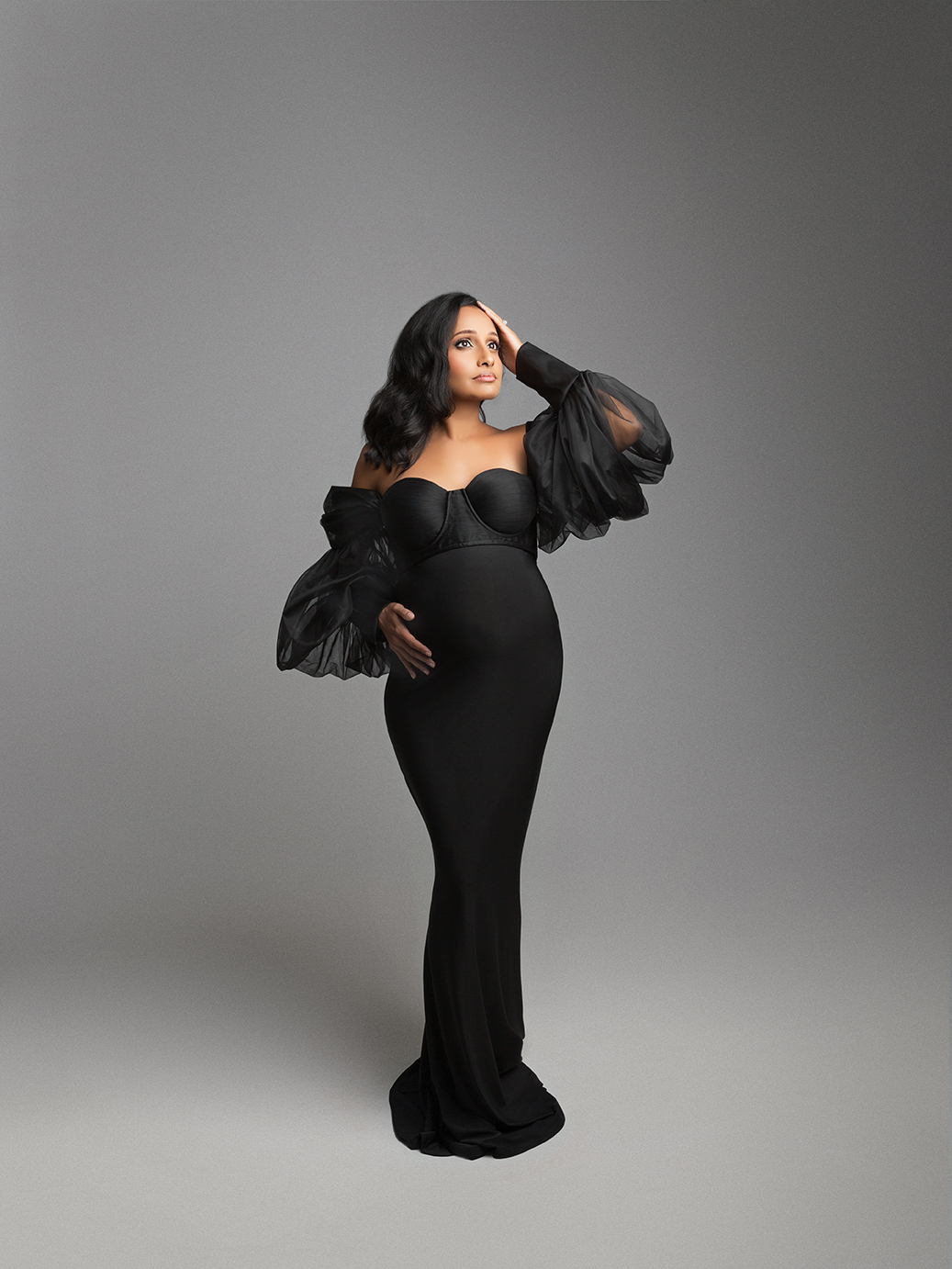 13ss Studio maternity portrait — pregnant woman in elegant black gown with dramatic sheer sleeves, modern and luxurious style