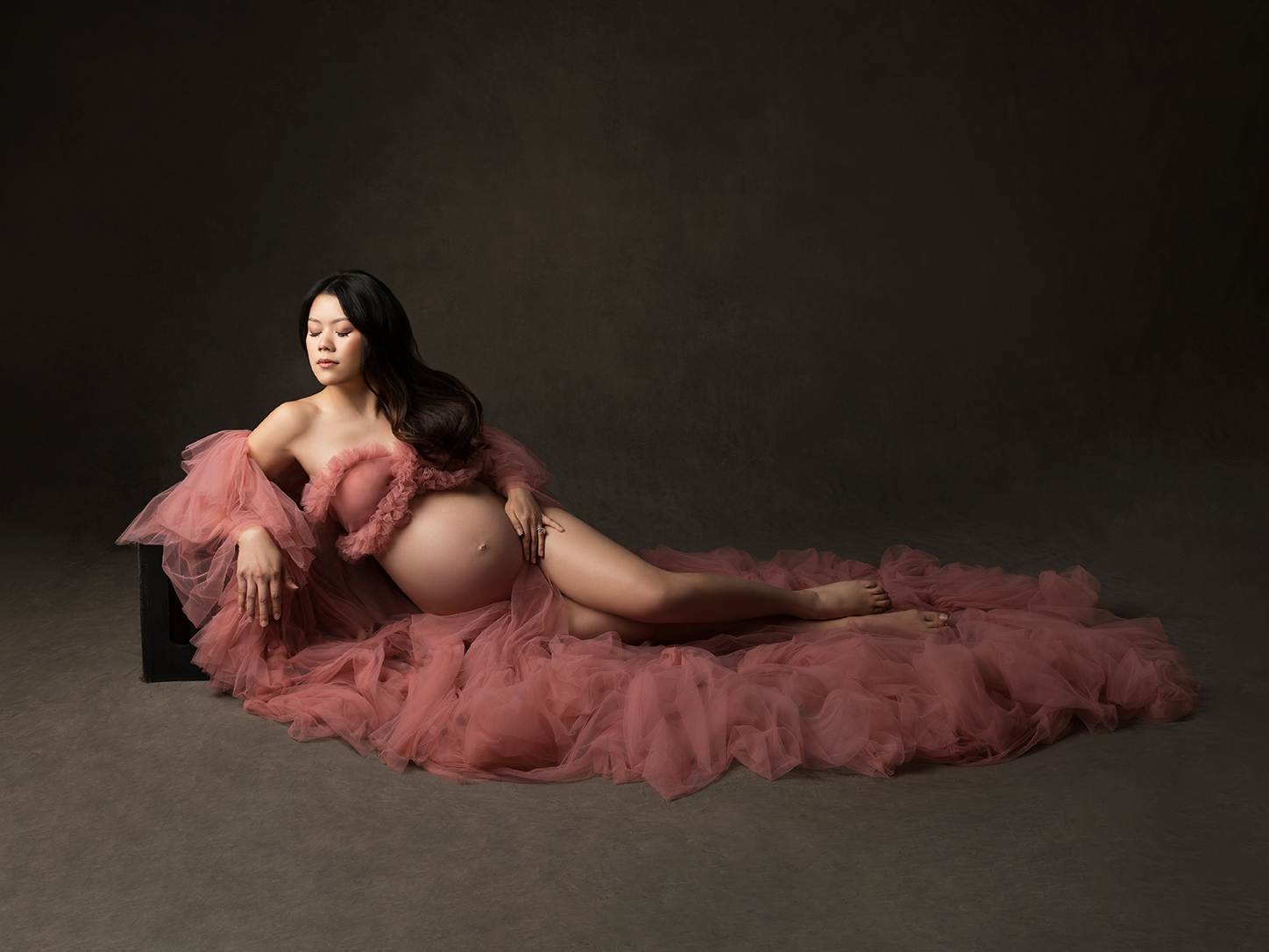 PixCake Elegant maternity portrait — pregnant woman reclining in blush pink tulle gown, fine art studio photography with soft, feminine style