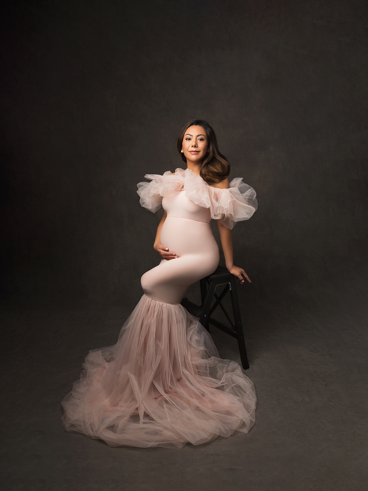 7s Studio maternity portrait — pregnant woman seated, fine art style with elegant and timeless beauty.