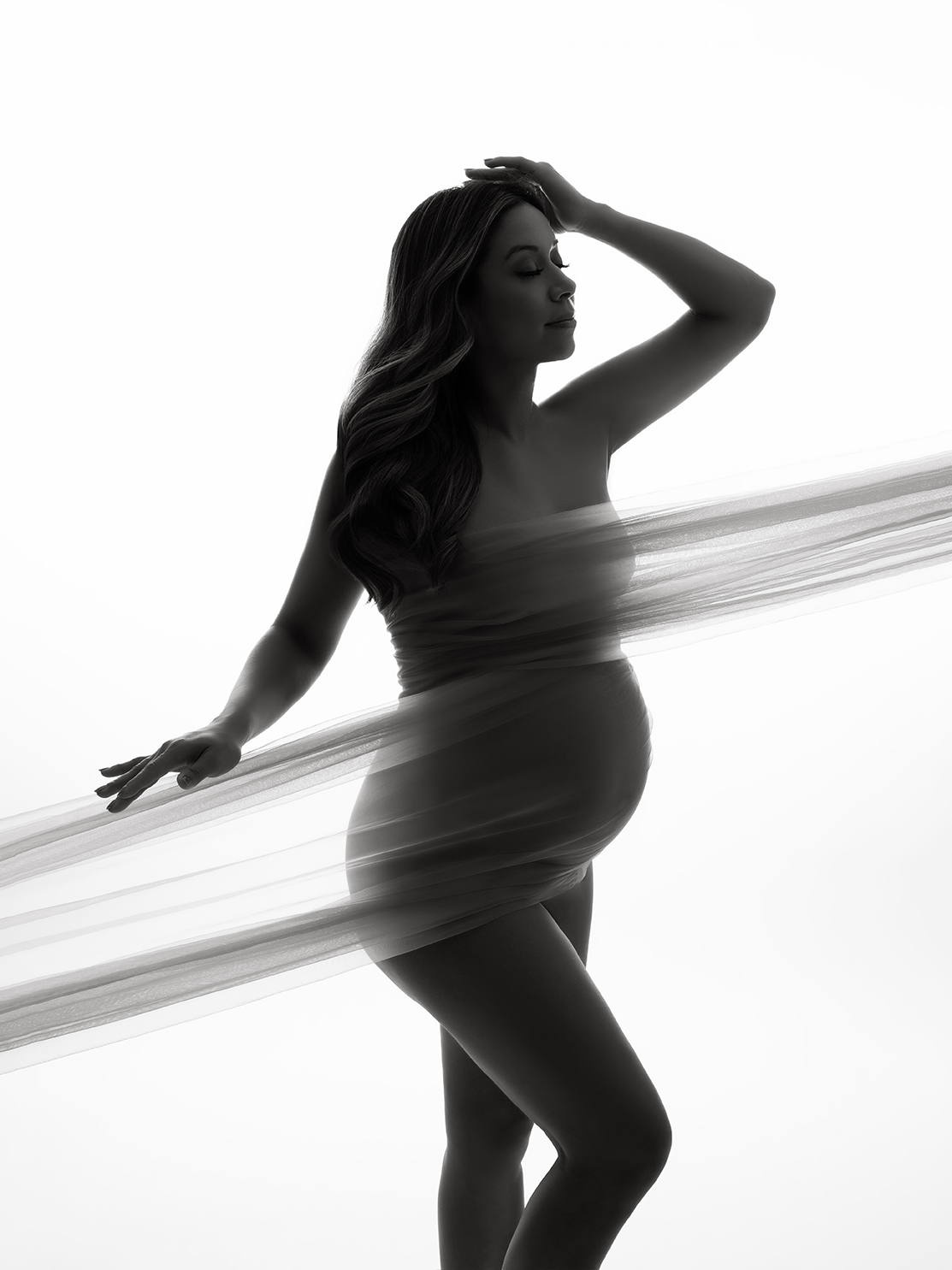 XIAOYUN PHOTOGRAPHY Backlit studio maternity portrait — pregnant woman draped in sheer fabric, soft silhouette with ethereal, minimalist style