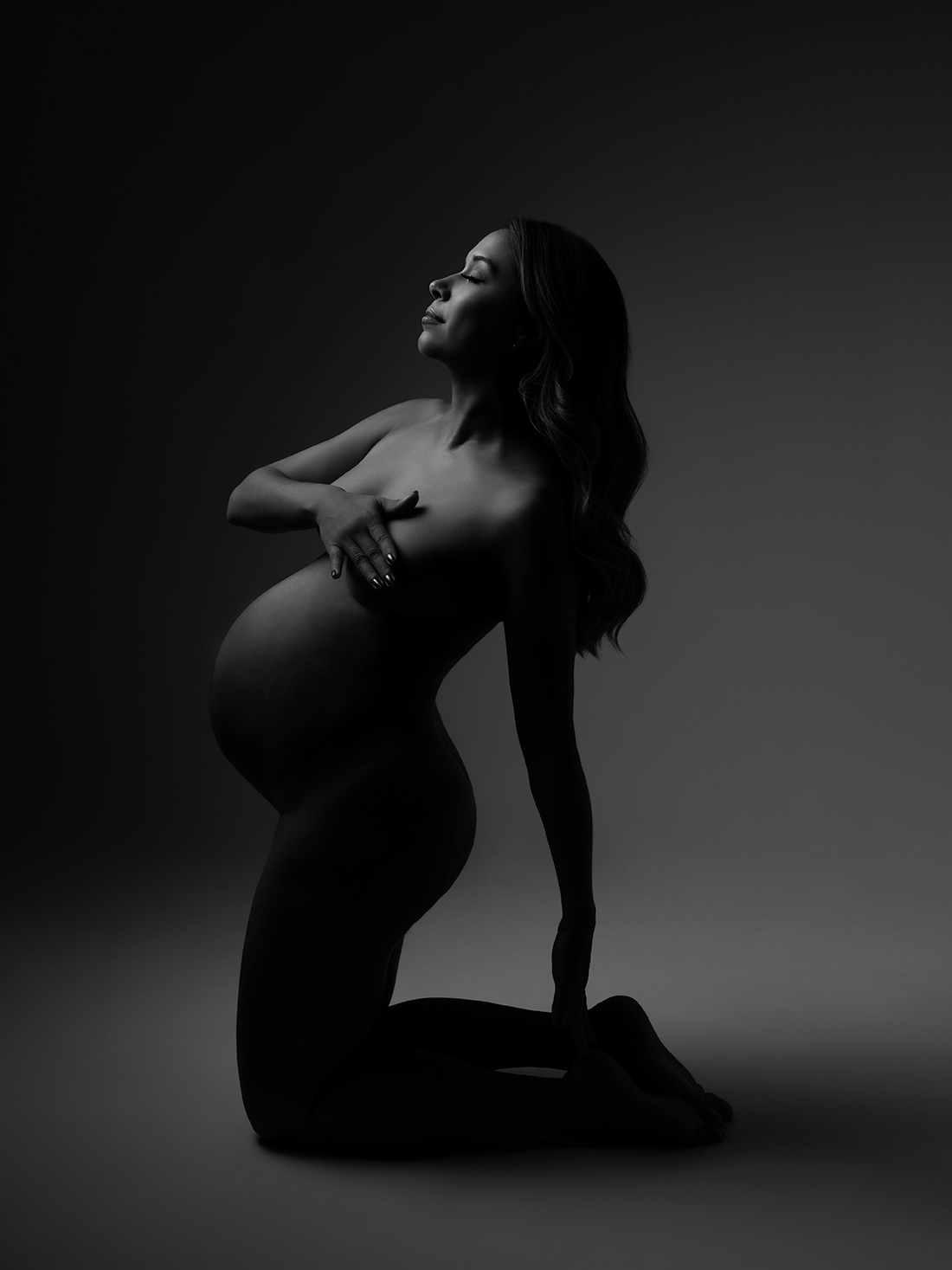 XIAOYUN PHOTOGRAPHY Fine art maternity portrait — pregnant woman in silhouette nude pose, kneeling with dramatic lighting, artistic maternity photography.