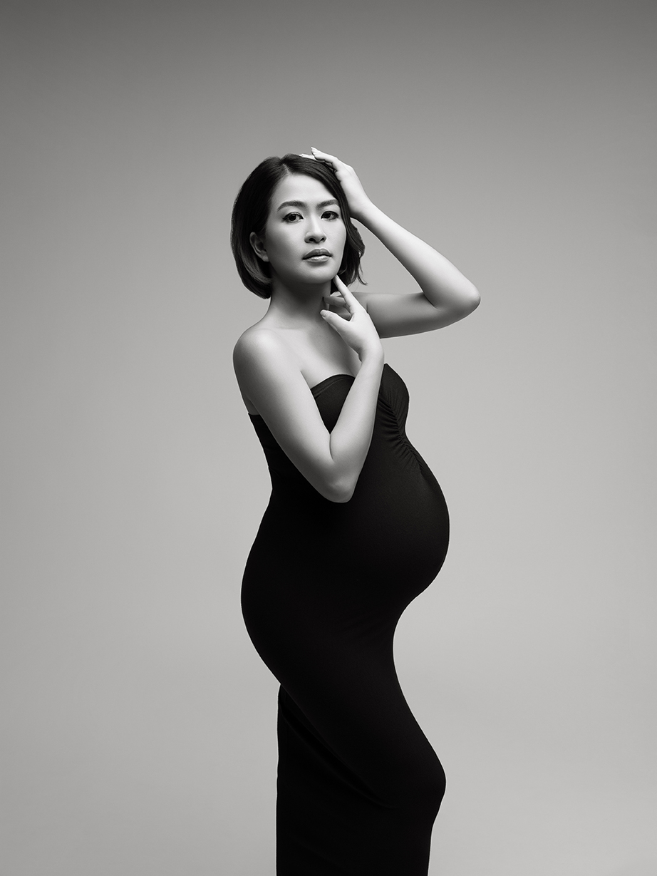 XIAOYUN PHOTOGRAPHY Black and white maternity portrait of pregnant woman in strapless black gown, posing in studio with editorial fashion look